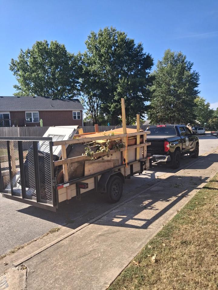 The Natural State Cleanout Co. truck towing a trailer stacked high with plywood, lumber, brush and an old door